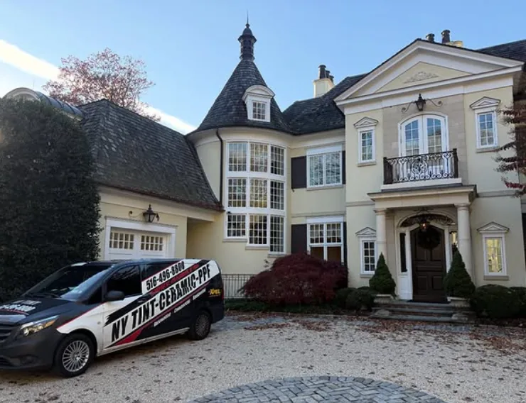 NY Window Tinting van parked in the gravel driveway of a large chateau-style Long Island home after a whole-house 70% ceramic film install
