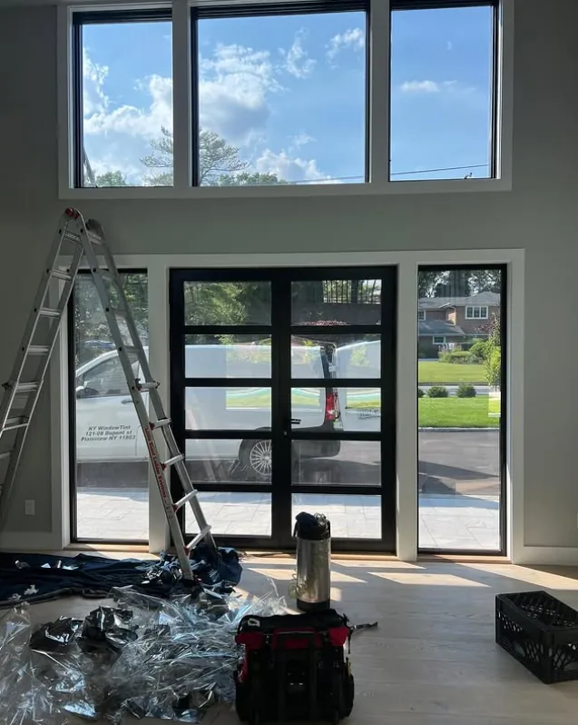 NY Window Tinting crew mid-install on a home's front entry glass, ladder and film tools in place