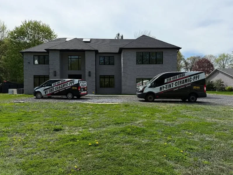 Two NY Window Tinting vans outside a modern home after a solar reflective window film install