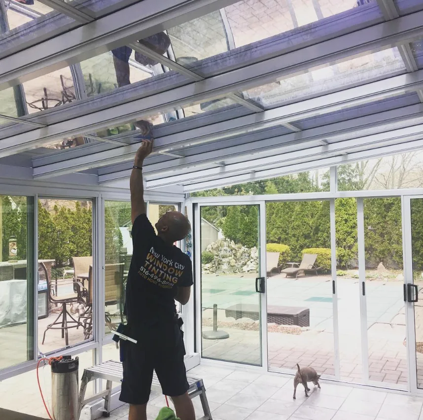 NY Window Tinting installer applying solar film to sunroom skylights at a customer's home